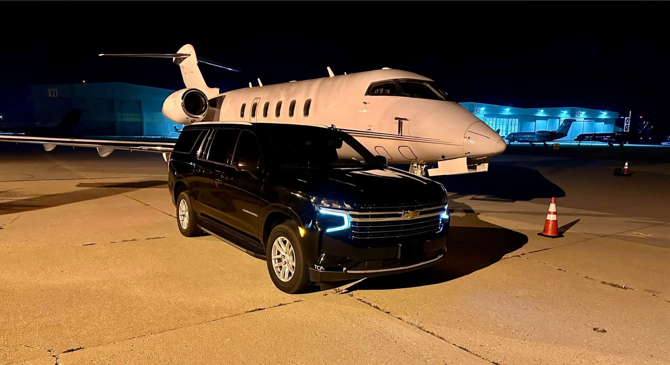 Black SUV beside a private jet at night